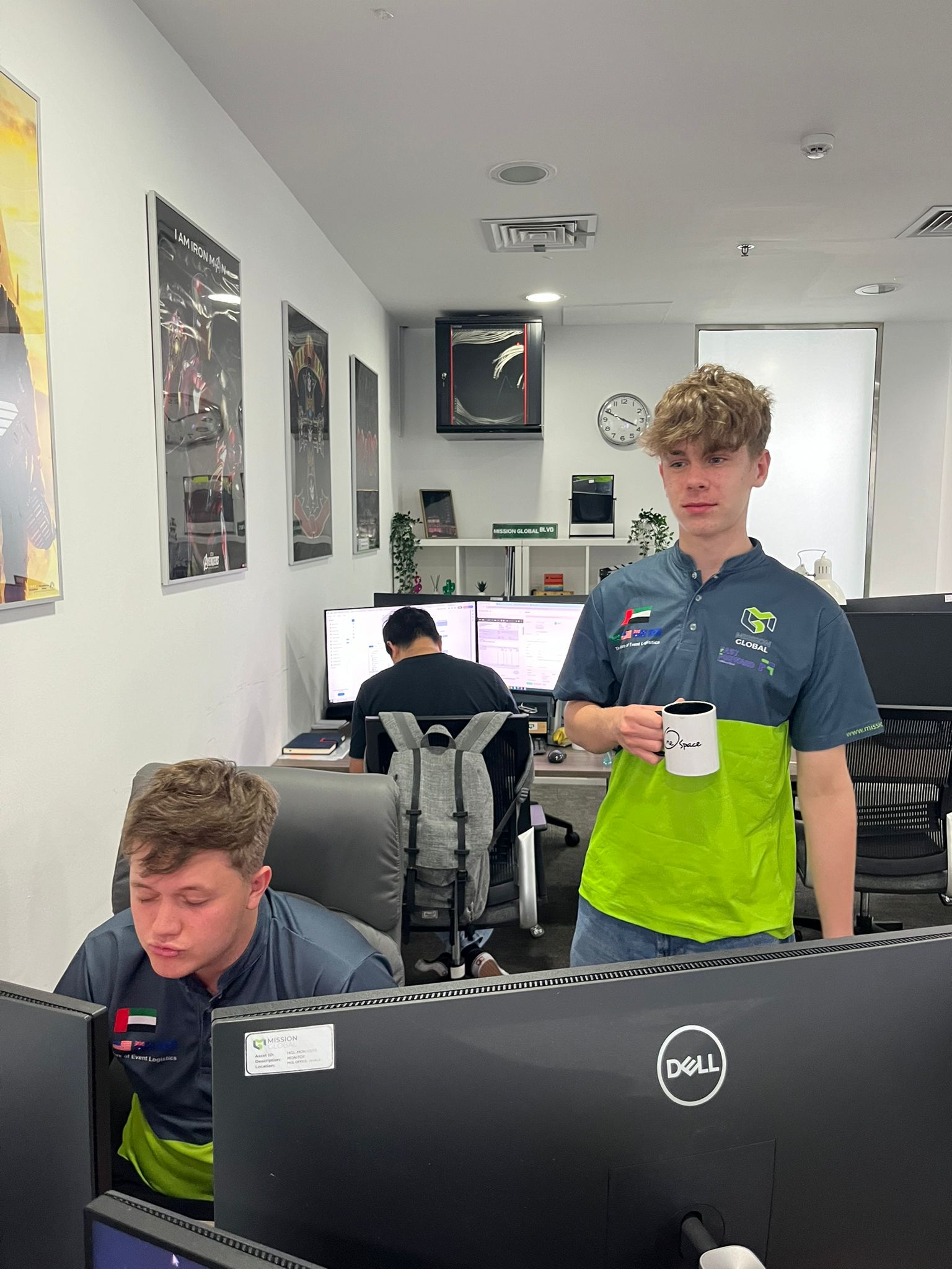 Will Hanlon standing with a mug in the Mission Global office in Dubai while colleagues work at nearby desks.